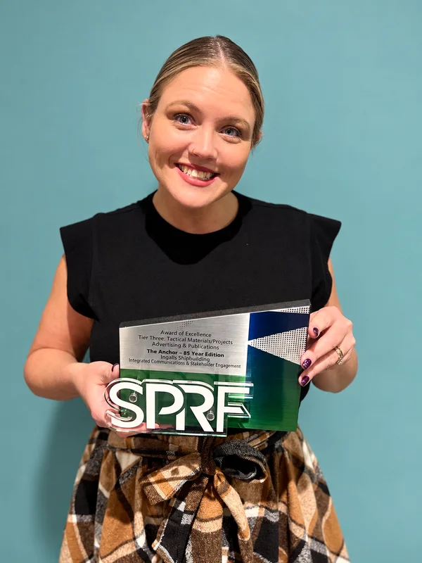 Lindsay Knowles smiles while holding her Southern Public Relations Federation Award of Excellence for The Anchor 85th anniversary edition